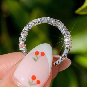 May include: A silver band ring with a row of small, clear diamonds set in a pave setting.