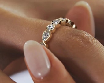 May include: A gold ring with a series of alternating round and pear-shaped clear gemstones. The ring is set in a yellow gold band. The gemstones are clear and sparkling, and the ring is shown on a finger.