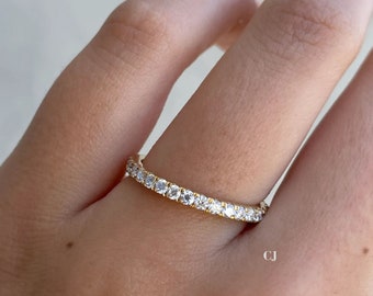 May include: A thin gold band with a row of small, clear diamonds.