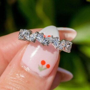 May include: A silver ring with a row of small, clear, pear-shaped stones set in a wavy pattern.