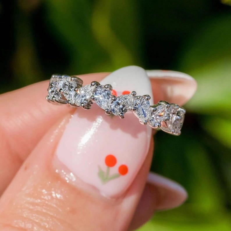 May include: A silver ring with a row of small, clear, pear-shaped stones set in a wavy pattern.