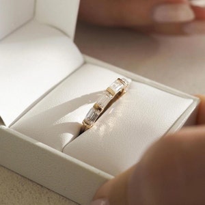 May include: A gold band with a row of baguette-cut diamonds set in a white box.