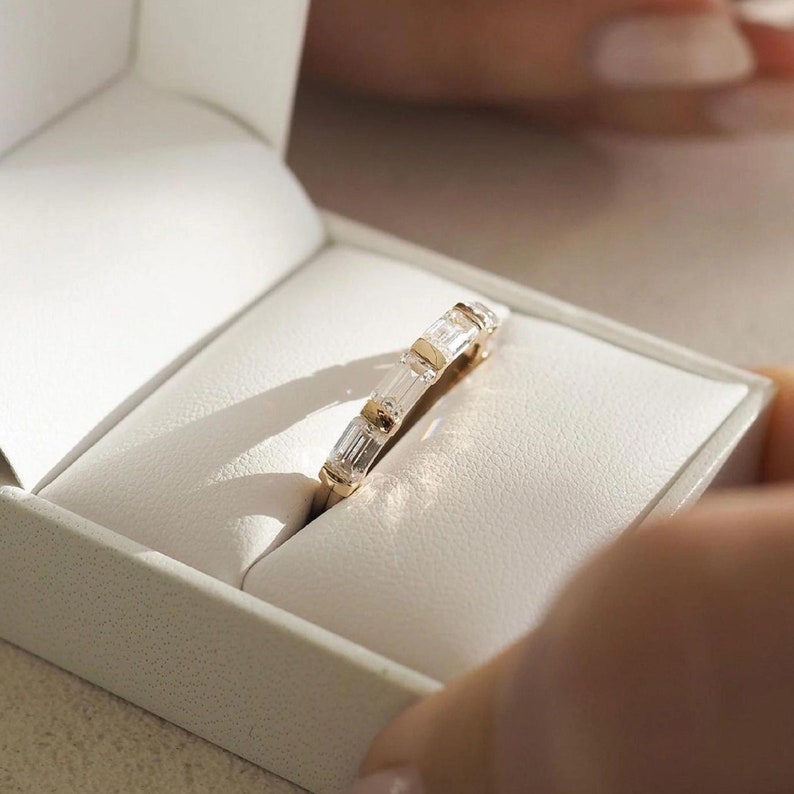 May include: A gold band with a row of baguette-cut diamonds set in a white box.