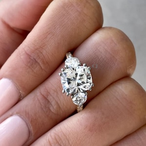 May include: A three-stone engagement ring featuring a large, square-shaped centre diamond and two smaller round diamonds on either side. The ring is set in a white gold band with a rose gold accent.