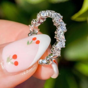 May include: A silver ring with a row of small, clear, triangular-shaped stones set in a delicate, curved band.