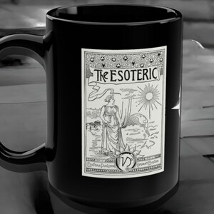 Può includere: Tazza in ceramica nera con una grafica bianca di una donna in piedi davanti a un sole e un globo. La grafica è circondata da un bordo con il testo "The Esoteric" e "Esoteric Publishing" e "Germany Boston".