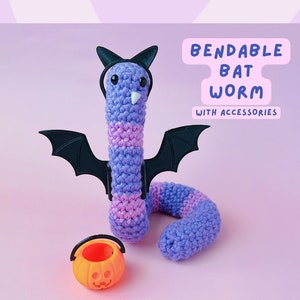 May include: A purple and pink crocheted worm wearing a black bat costume and holding a small orange pumpkin bucket. The text "Bendable Bat Worm with Accessories" is written in white on a pink background.