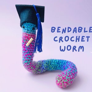 May include: A colorful crocheted worm wearing a black graduation cap with a blue tassel. The worm is holding a small scroll in its hand. The text "Bendable Crochet Worm" is written in blue letters on a white background.