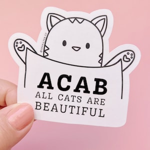 May include: White sticker with a black line drawing of a cat peeking out of a pocket. The text reads "ACAB ALL CATS ARE BEAUTIFUL".