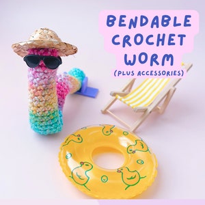 May include: A colorful crocheted worm wearing sunglasses and a straw hat, sitting on a pink surface with a yellow inflatable ring and a striped beach chair. The text "Bendable Crochet Worm (Plus Accessories)" is written above the worm.