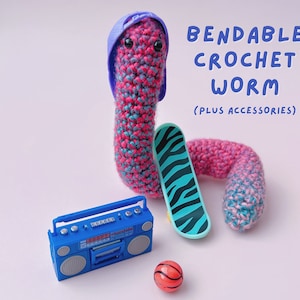 May include: A pink and blue crocheted worm wearing a purple hat and holding a blue and white skateboard. The worm is also next to a blue boombox and an orange basketball.