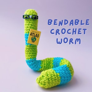 May include: A green and blue crocheted worm toy with glasses and a yellow book that says "WORLD ATLAS". The worm is bendable and is a crochet craft.