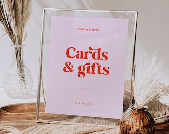 May include: A silver frame with a pink card inside. The card says "Paloma & Jacob Cards & gifts Thank You!" in red text. The frame is sitting on a wooden table with a beige fabric runner.