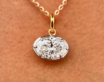 May include: A gold necklace with an oval-shaped diamond pendant. The diamond is set in a silver-colored bezel and sparkles brightly. The chain is delicate and gold. The pendant is centered in the frame, showcasing the jewelry.