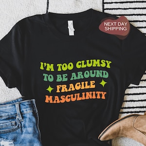 Peut inclure: T-shirt noir avec un graphisme rétro qui dit "Je suis trop maladroit pour être autour de la masculinité fragile".