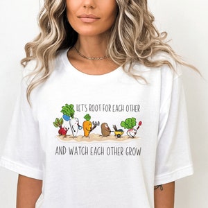 May include: White t-shirt with a graphic of cartoon vegetables and the text "Let's root for each other and watch each other grow."