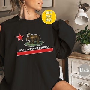 Peut inclure: Sweat-shirt noir avec un graphique du drapeau de la R&eacute;publique de Californie repr&eacute;sentant deux ours et une &eacute;toile rouge. Le texte "NEW CALIFORNIA REPUBLIC" est imprim&eacute; sous le drapeau.