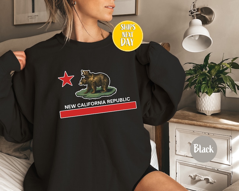 Peut inclure: Sweat-shirt noir avec un graphique du drapeau de la R&eacute;publique de Californie repr&eacute;sentant deux ours et une &eacute;toile rouge. Le texte "NEW CALIFORNIA REPUBLIC" est imprim&eacute; sous le drapeau.
