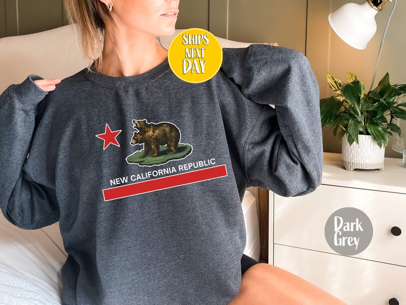 Peut inclure: Sweat-shirt gris fonc&eacute; avec un graphique du drapeau de l'&Eacute;tat de Californie repr&eacute;sentant deux ours et une &eacute;toile rouge. Le texte "NEW CALIFORNIA REPUBLIC" est imprim&eacute; sous le drapeau.