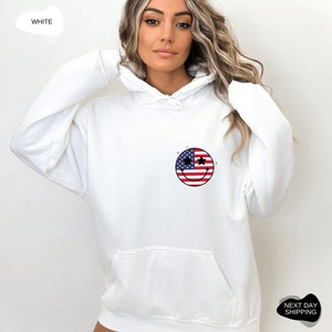 May include: White hooded sweatshirt with a smiley face design featuring the American flag. The smiley face has stars for eyes.