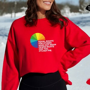 Op de afbeelding: Rood sweatshirt met een regenboogtaart-afbeelding en de tekst "Gelijke rechten voor anderen betekent niet minder rechten voor jou. Het is geen taart."