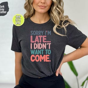 May include: Dark grey heather t-shirt with the text "SORRY I'M LATE... I DIDN'T WANT TO COME." in colorful letters.