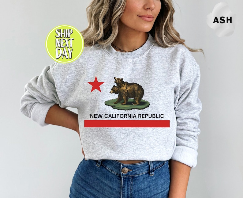Peut inclure: Un sweat-shirt gris avec une &eacute;toile rouge et deux ours bruns sur une colline verte. Le texte "NEW CALIFORNIA REPUBLIC" est imprim&eacute; sous les ours.