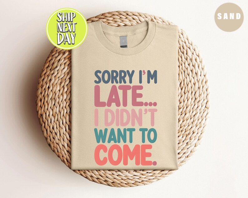 May include: A beige t-shirt with the text "Sorry I'm Late... I Didn't Want To Come." in colorful letters.