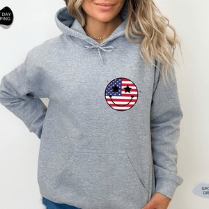 May include: A gray hooded sweatshirt with a smiley face design featuring the American flag. The smiley face has stars for eyes.