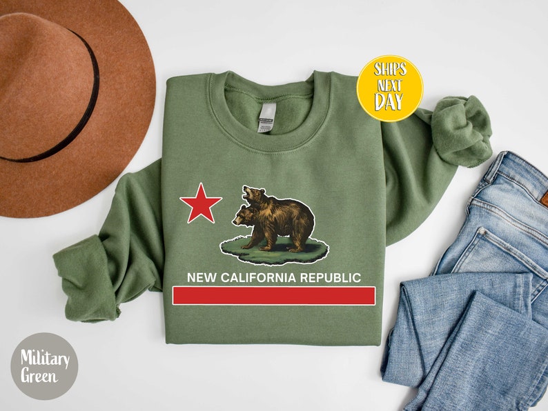 Peut inclure: Un sweat-shirt vert militaire avec une &eacute;toile rouge et deux ours bruns imprim&eacute;s sur le devant. Le texte "NEW CALIFORNIA REPUBLIC" est imprim&eacute; sous les ours.