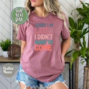 May include: A heather mauve t-shirt with the text "Sorry I'm Late I Didn't Want To Come." in colorful, stylized lettering.