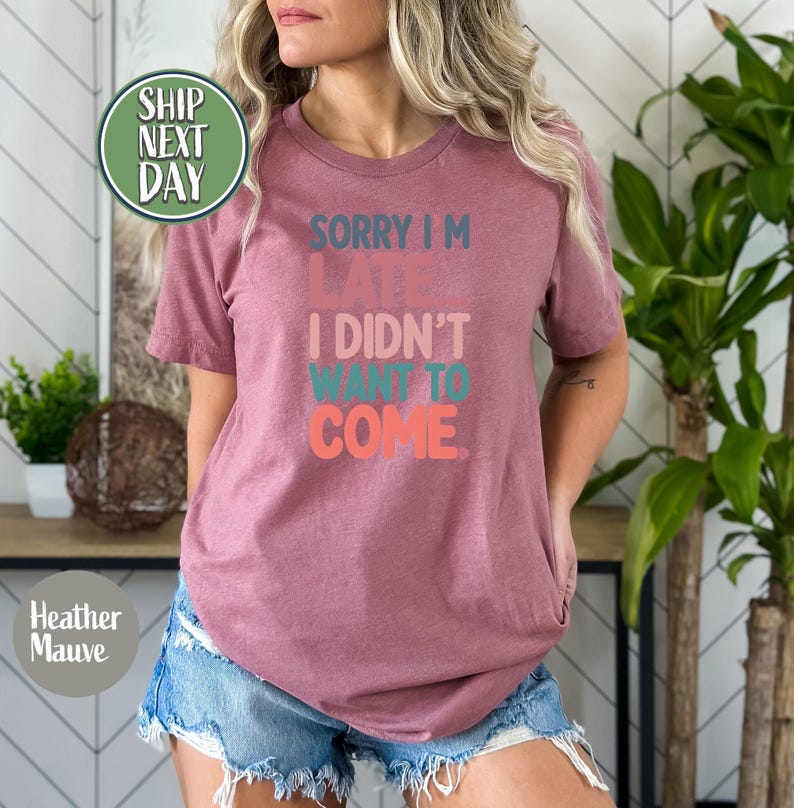 May include: A heather mauve t-shirt with the text "Sorry I'm Late I Didn't Want To Come." in colorful, stylized lettering.