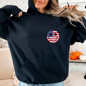 May include: Black hoodie with a smiley face design featuring the American flag. The stars on the smiley face are black.