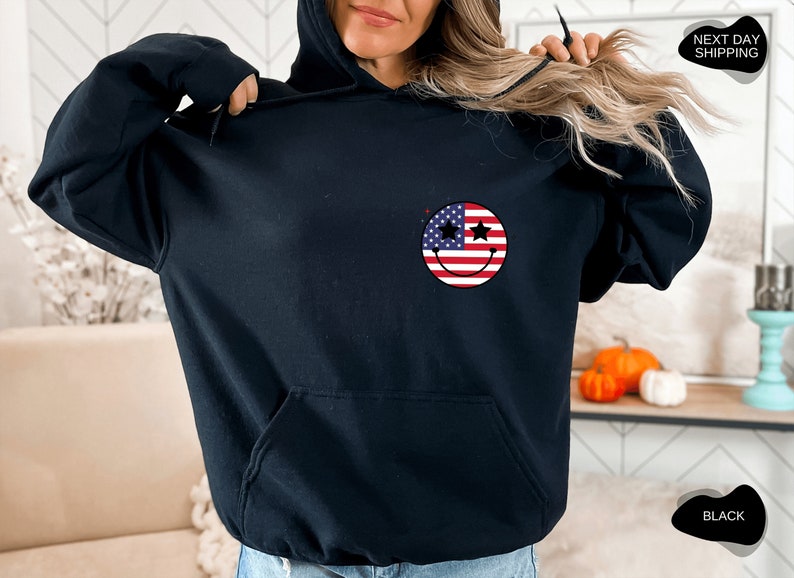 May include: Black hoodie with a smiley face design featuring the American flag. The stars on the smiley face are black.