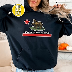 Peut inclure: Sweat-shirt &agrave; capuche noir avec un graphique du drapeau de la R&eacute;publique de Californie repr&eacute;sentant deux ours et le texte "New California Republic".