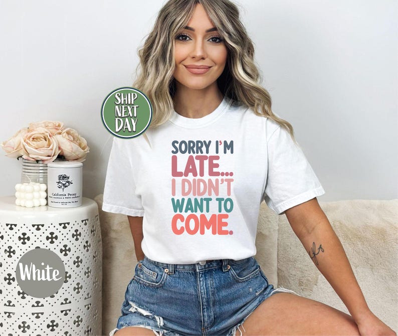 May include: White t-shirt with the text "Sorry I'm Late... I Didn't Want To Come." printed in colorful letters. The shirt is being worn by a person with long blonde hair.
