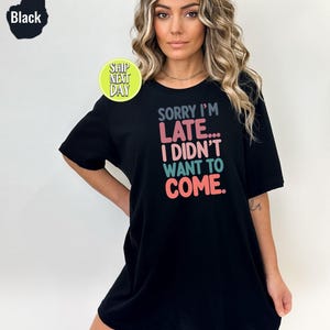 May include: Black t-shirt with the text "SORRY I'M LATE... I DIDN'T WANT TO COME." in colorful letters.