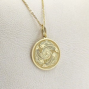 May include: A gold necklace with a round pendant featuring a detailed engraved design of a spiral with three fish. The pendant is on a white background.