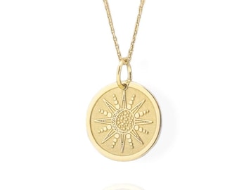 May include: A gold necklace with a round pendant featuring a sun design. The pendant has a textured surface and a raised sun design.