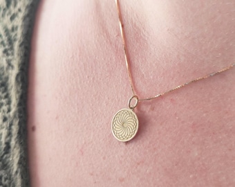 Könnte beinhalten: Eine goldene Kettenkette mit einem runden Anhänger mit geometrischem Muster.