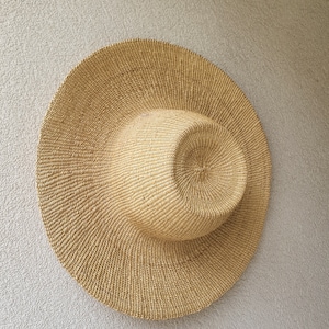 May include: A large, round, woven straw hat with a wide brim. The hat is light brown in color and has a slightly textured surface.