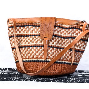 May include: Woven shoulder bag with a geometric pattern in brown, cream, and black. The bag has a leather flap closure and adjustable leather shoulder strap. A stylish accessory.