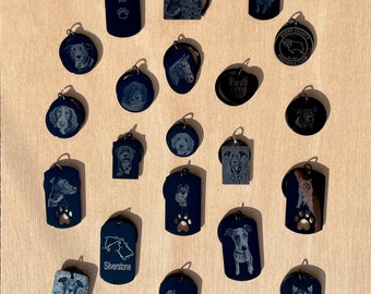 May include: A collection of black metal keychains with various designs, including animals, logos, and text. Some keychains feature engraved images of dogs, horses, and a football club logo. Others have text like "In Memory Of", "Silverstone", "Pip", and "Teddy".