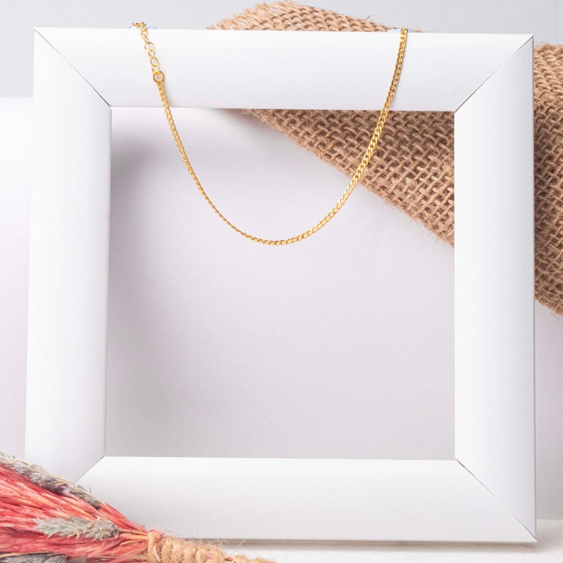 May include: A gold chain necklace displayed in a white frame. The chain is delicate and has a subtle shine.