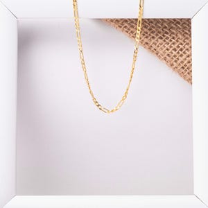 May include: A gold chain necklace with a delicate, flat, link design. The chain is displayed on a white background with a piece of burlap fabric.