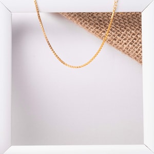 May include: A gold chain necklace on a white background with a piece of burlap fabric.