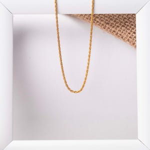 May include: A gold rope chain necklace on a white background.