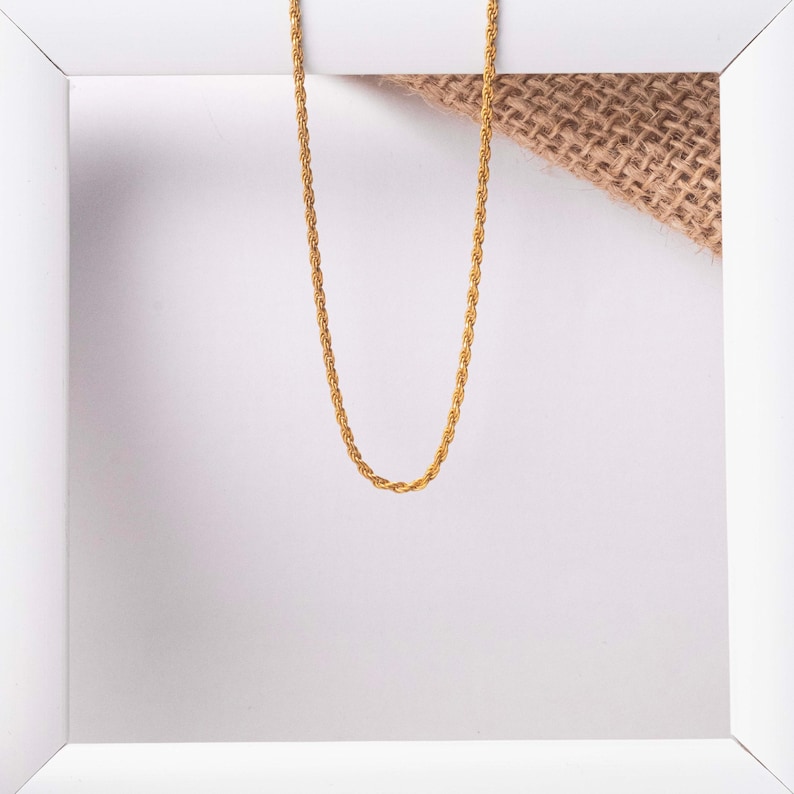 May include: A gold rope chain necklace on a white background.