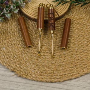 Puede incluir: Un juego de dos herramientas de madera y doradas con estuches a juego. Una herramienta tiene las iniciales "T&K" grabadas. Las herramientas tienen un extremo en forma de cuchara y un extremo puntiagudo. Los estuches son cilíndricos y de madera.