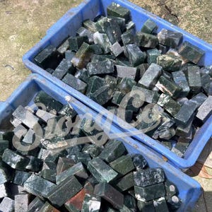 以下が含まれることがあります： 2つの青いプラスチック製の容器に、粗くカットされた長方形の石が詰められています。石は主に濃い緑色で、より明るい緑色と灰色のマーブル模様があります。石は生のままで研磨されておらず、自然な質感の表面を持っています。
